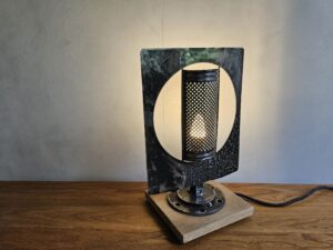 Lampe récup en métal noir et socle en bois, abat-jour rectangulaire avec grand disque crème au centre et lumière chaude.